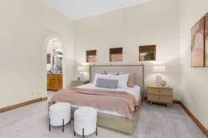 Bedroom featuring ensuite bath, arched walkways, and light carpet