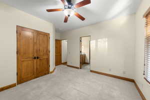Unfurnished bedroom with connected bathroom, ceiling fan, light carpet, a closet, and multiple windows