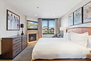 Bedroom with light carpet, a glass covered fireplace, and recessed lighting