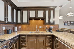 Kitchen featuring dark brown cabinetry, backsplash, light stone countertops, and appliances with stainless steel finishes