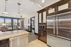 Kitchen with dark brown cabinetry, built in appliances, decorative light fixtures, light stone counters, and recessed lighting