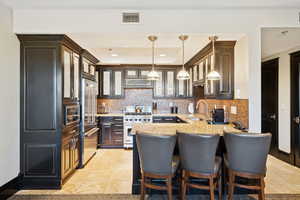 Kitchen with decorative backsplash, a kitchen bar, glass insert cabinets, pendant lighting, and premium appliances