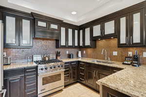 Kitchen featuring glass insert cabinets, designer range, tasteful backsplash, dark brown cabinetry, and recessed lighting