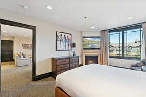 Carpeted bedroom with a glass covered fireplace and recessed lighting
