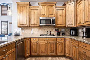 Kitchen with stainless steel appliances, brown cabinets, light stone counters, and light wood-type flooring