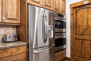 Kitchen featuring stainless steel appliances, brown cabinets, backsplash, and light stone countertops