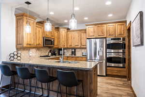 Kitchen with appliances with stainless steel finishes, recessed lighting, a kitchen bar, light stone counters, and a peninsula