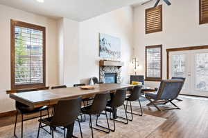 Dining room featuring a stone fireplace, french doors, wood finished floors, and a towering ceiling