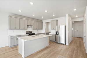 **DISCLAIMER - INTERIOR & EXTERIOR options may vary.Kitchen featuring backsplash, appliances with stainless steel finishes, gray cabinets, an island with sink, and light wood-type flooring