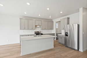 Kitchen with appliances with stainless steel finishes, gray cabinets, backsplash, an island with sink, and recessed lighting