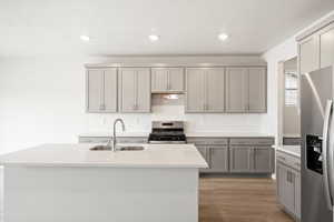 **DISCLAIMER - INTERIOR & EXTERIOR options may vary. Kitchen with appliances with stainless steel finishes, decorative backsplash, gray cabinetry, light stone counters, and a kitchen island with sink