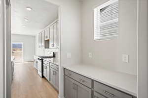 Kitchen with stainless steel range with gas stovetop, gray cabinets, light wood-type flooring, backsplash, and light stone countertops