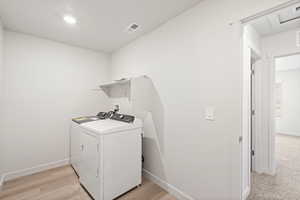 Laundry area with independent washer and dryer, light wood-style floors, and recessed lighting