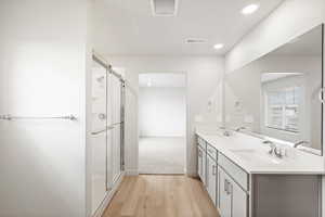 Full bath with light wood-style flooring, double vanity, recessed lighting, and a stall shower