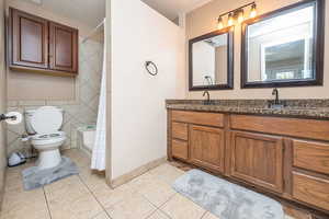 Full bath with double vanity, light tile patterned flooring, tile walls, shower / bath combination with curtain, and a textured ceiling