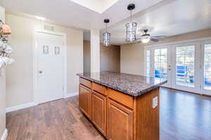 Kitchen with brown cabinetry, hanging light fixtures, a center island, french doors, and dark wood-style floors