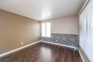 Unfurnished room featuring a textured ceiling, dark wood-style flooring, and wainscoting