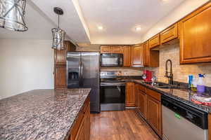 Kitchen with appliances with stainless steel finishes, decorative backsplash, dark stone countertops, brown cabinets, and pendant lighting