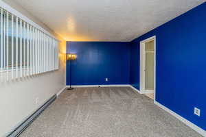 Empty room featuring a baseboard heating unit, a textured ceiling, and light carpet