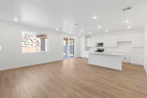 Kitchen featuring a kitchen island with sink, white cabinetry, recessed lighting, open floor plan, and light wood-type flooring