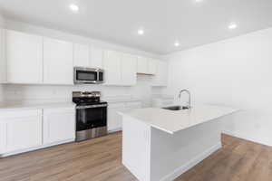 Kitchen featuring stainless steel appliances, white cabinets, light stone counters, light wood-style floors, and a kitchen island with sink