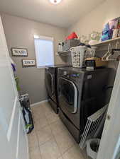 Laundry area with a textured ceiling, washer and dryer, and light tile patterned floors