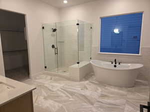 Full Main bathroom featuring a freestanding tub, a stall shower, tile walls, a walk in closet, and vanity