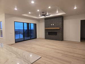 Unfurnished living room with a ceiling fan, light wood finished floors, recessed lighting, a raised ceiling, and a large fireplace