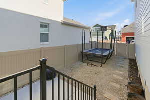 Full vinyl fencing with double gates opening up to a zero-scape backyard with a trampoline