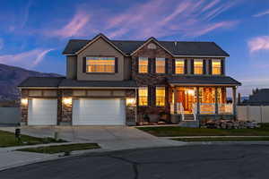 View of front of property with stone siding, driveway, covered porch, an attached garage, and a tiled roof