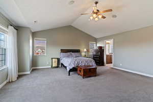 Bedroom with vaulted ceiling, multiple windows, carpet floors, a ceiling fan, and ensuite bath