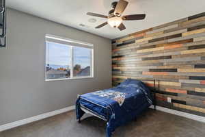Carpeted bedroom with wooden walls, a ceiling fan, and a mountain view