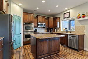 Kitchen featuring stainless steel appliances, a kitchen island, tasteful backsplash, recessed lighting, and light stone counters