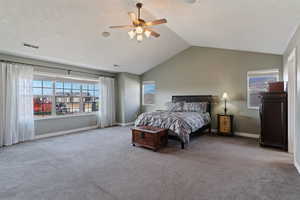 Carpeted bedroom featuring multiple windows, vaulted ceiling, and a ceiling fan