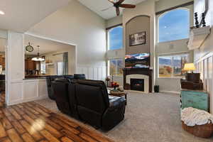 Carpeted living area with a ceiling fan, a towering ceiling, a tiled fireplace, a decorative wall, and a chandelier