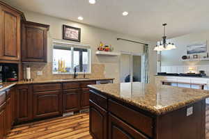 Kitchen with dark brown cabinetry, light stone counters, a center island, light wood-style floors, and recessed lighting