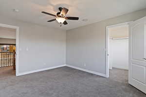 Unfurnished bedroom featuring light colored carpet, a spacious closet, and a ceiling fan