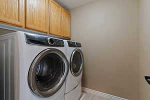 Laundry area featuring light tile patterned floors, washing machine and dryer, and cabinet space