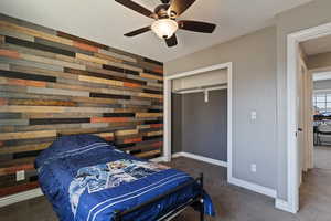 Carpeted bedroom with wood walls, a ceiling fan, and a closet