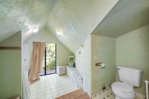 Bathroom featuring a textured ceiling, vaulted ceiling, shower / tub combo, and tile patterned floors