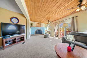Carpeted living room with a fireplace, wooden ceiling, and ceiling fan