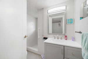 Bathroom with tile walls, vanity, a walk in shower, and light tile patterned floors