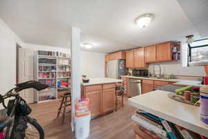 Kitchen featuring light countertops, light wood-style floors, open shelves, a textured ceiling, and appliances with stainless steel finishes