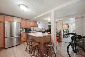 Kitchen featuring stainless steel appliances, light countertops, light wood-style flooring, a textured ceiling, and a kitchen island