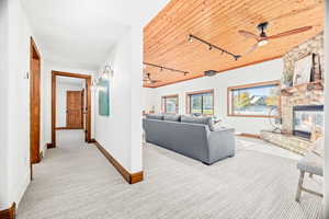 Living room featuring rail lighting, carpet flooring, wood ceiling, a stone fireplace, and ceiling fan