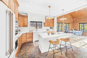 Kitchen featuring vaulted ceiling, log walls, a breakfast bar, decorative light fixtures, and recessed lighting