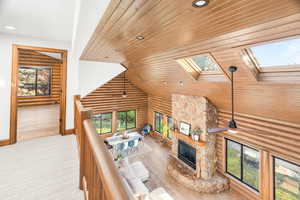 Living room featuring wooden ceiling, a stone fireplace, recessed lighting, a skylight, and rustic walls