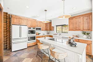 Kitchen with white appliances, a breakfast bar area, pendant lighting, dark stone finish floors, and recessed lighting
