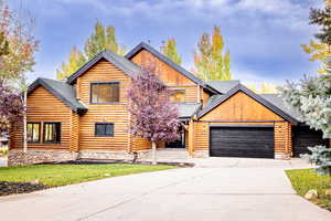 Log-style house featuring log exterior, driveway, a front yard, roof with shingles, and a garage