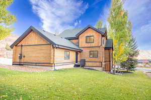 Back of house with log exterior, a lawn, and a shingled roof